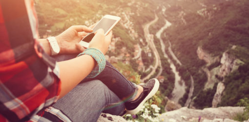 A woman sits at a scenic outlook using her phone.