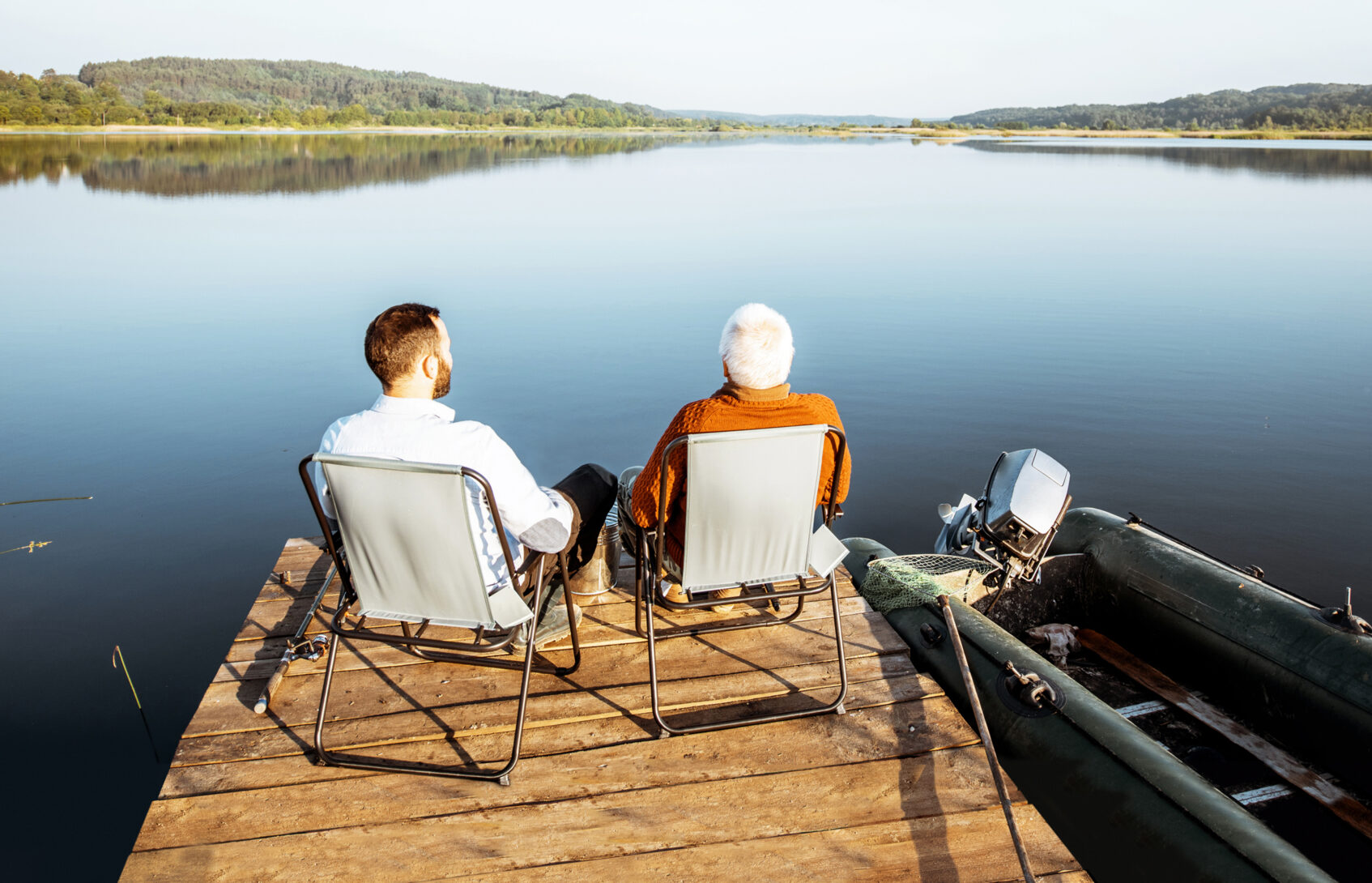 Father and son sitting on a dock at the edge of a lake talking
