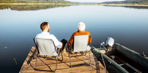Father and son sitting on a dock at the edge of a lake talking