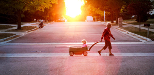 A grandparent pulls a young child in a wagon across the street