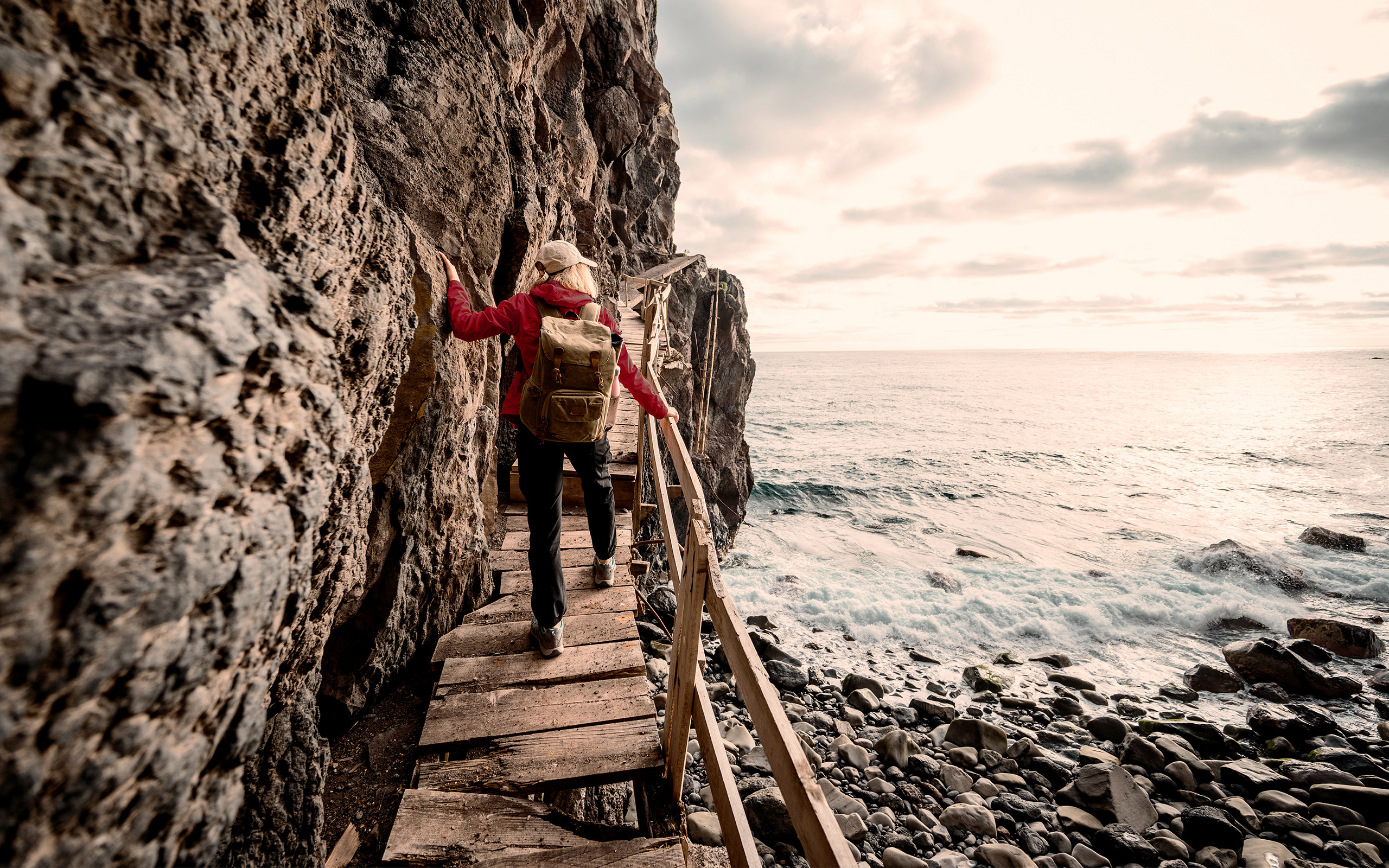 A woman uses a handrail in climbing a wooden ramp by an ocean cliff.