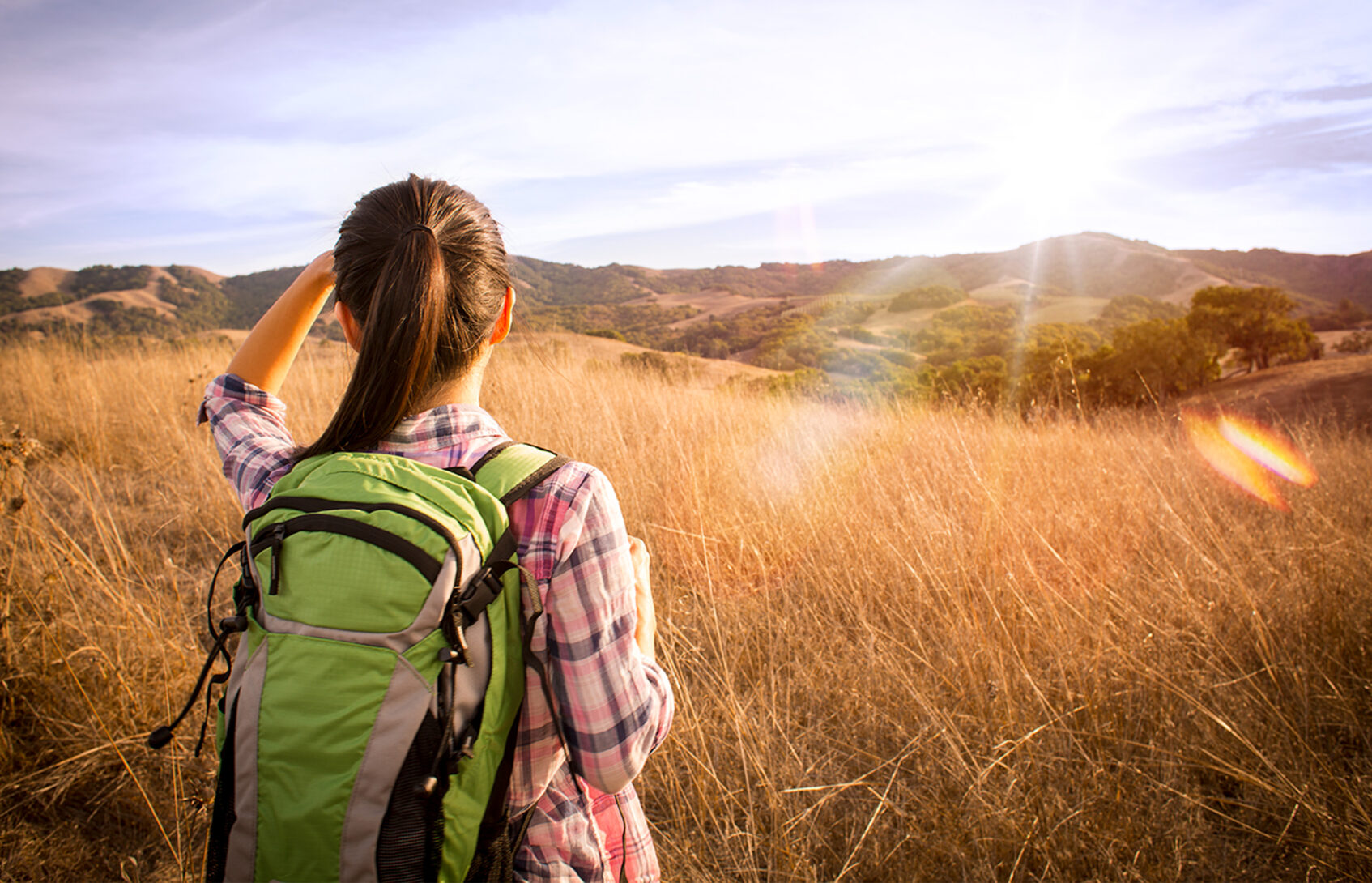 A woman wearing a backpack looks out over a field.