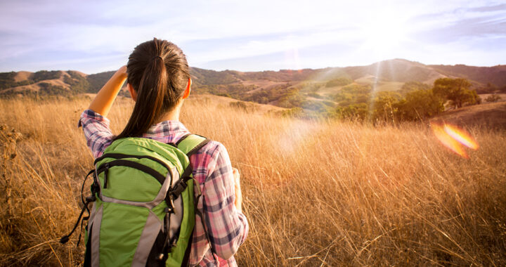 A woman wearing a backpack looks out over a field.